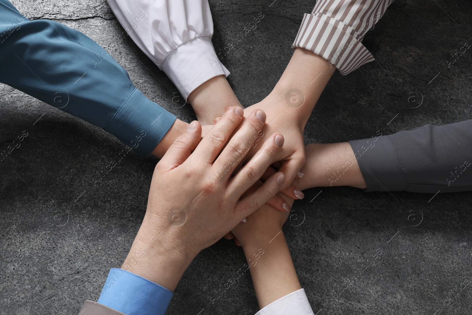 Photo of Business concept. Group of people stacking hands at grey textured table, top view