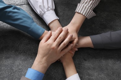 Business concept. Group of people stacking hands at grey textured table, top view