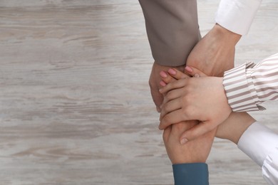 Photo of Business concept. Group of people stacking hands at light wooden table, top view. Space for text