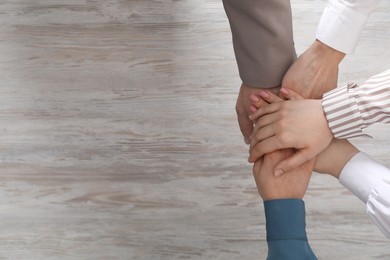 Photo of Business concept. Group of people stacking hands at light wooden table, top view. Space for text