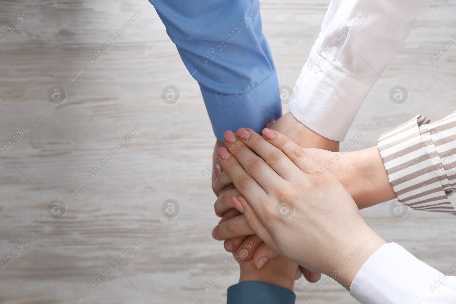 Photo of Business concept. Group of people stacking hands at light wooden table, top view. Space for text