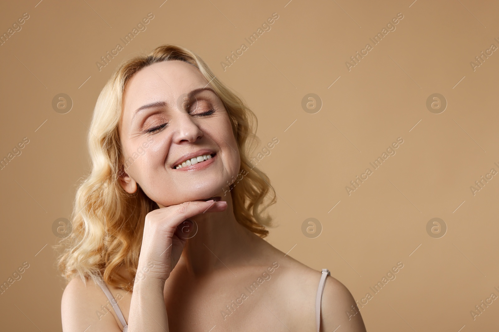 Photo of Smiling middle aged woman on beige background. Space for text