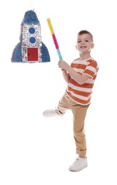 Photo of Happy boy breaking rocket shaped pinata with stick on white background