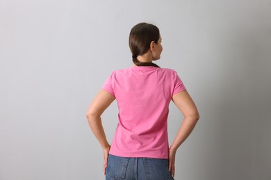 Photo of Woman in pink t-shirt on grey background, back view. Mockup for design