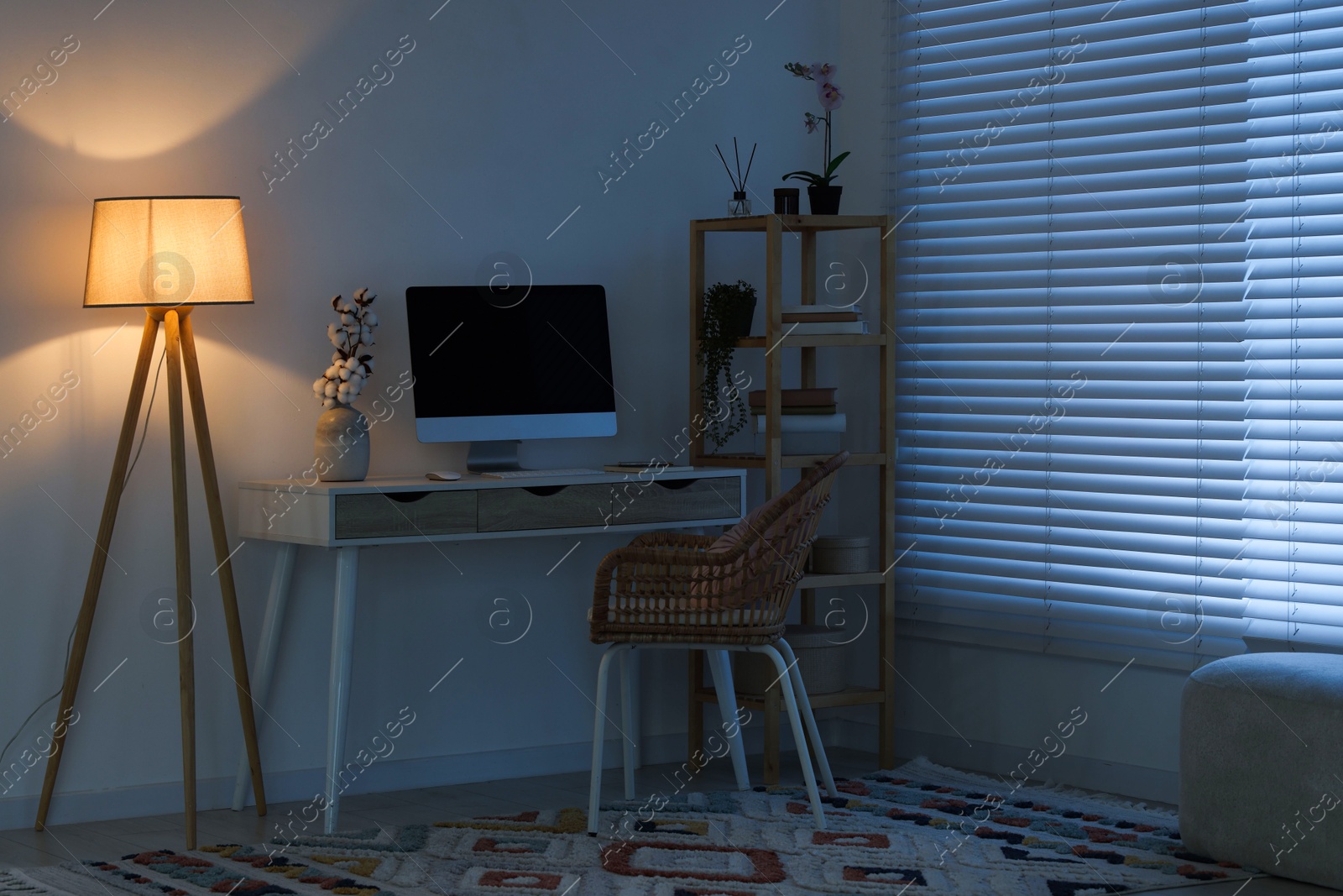 Comfortable workplace with computer on desk and floor lamp at home office in evening Photo of Comfortable workplace with computer on desk and floor lamp at home office in evening