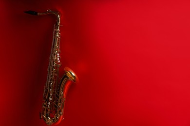 Photo of Jazz. One beautiful saxophone on red background, space for text