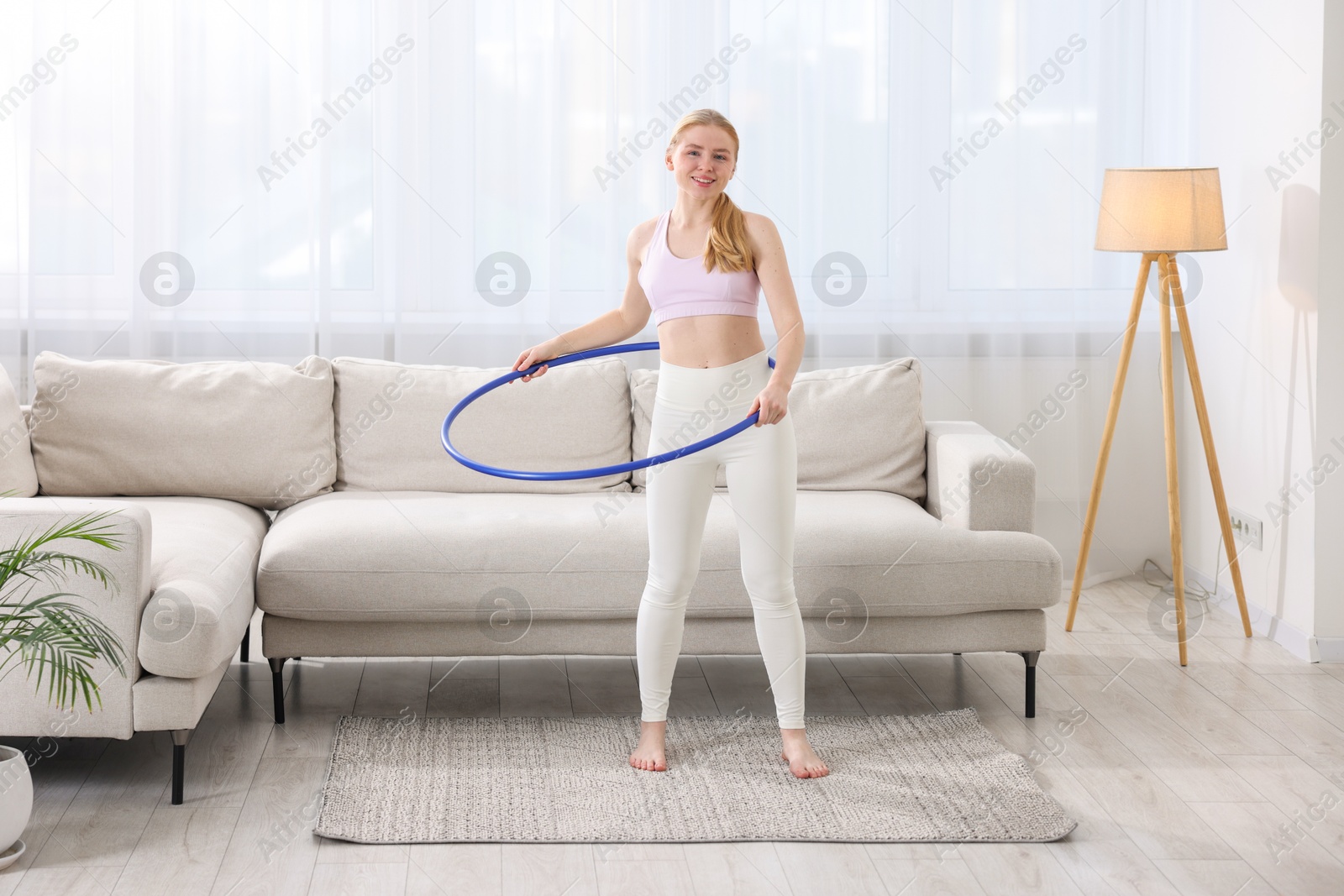 Photo of Beautiful young woman exercising with hula hoop at home