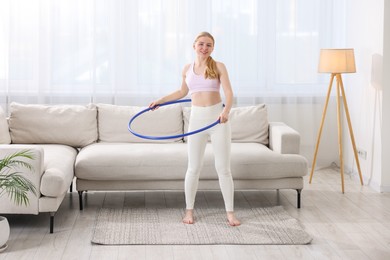 Beautiful young woman exercising with hula hoop at home