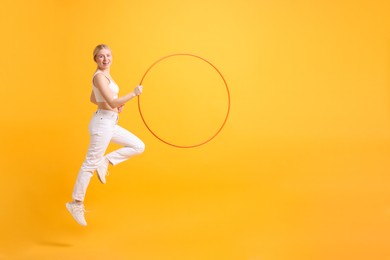 Beautiful young woman exercising with hula hoop on yellow background, space for text