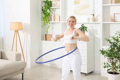 Beautiful young woman exercising with hula hoop at home