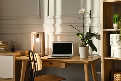 Photo of Comfortable workplace with modern laptop and lamp on wooden desk in home office