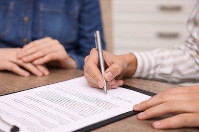 Photo of Man putting signature on document at table, closeup