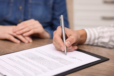 Photo of Man putting signature on document at table, closeup