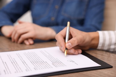 Photo of Man putting signature on document at table, closeup