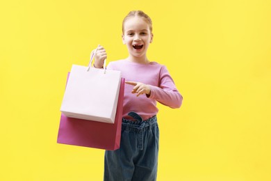 Cute little girl pointing at shopping bags on yellow background