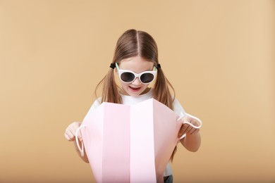 Cute little girl with shopping bag on beige background