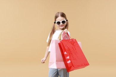 Cute little girl with shopping bags on beige background