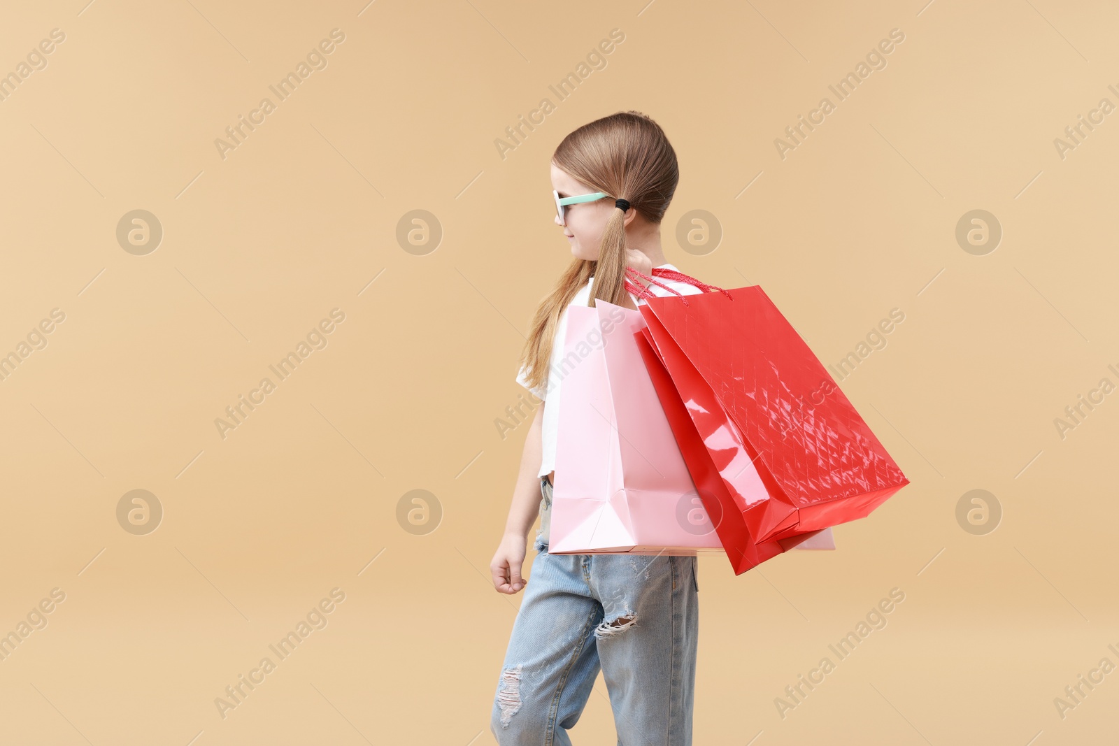 Photo of Cute little girl with shopping bags on beige background. Space for text