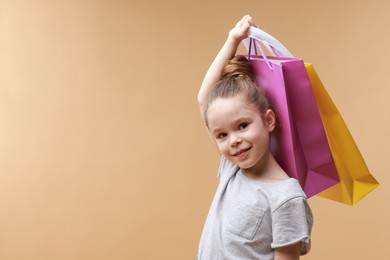 Photo of Happy little girl with shopping bags on beige background. Space for text