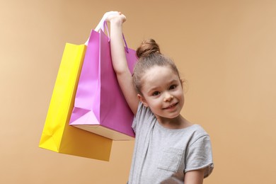 Photo of Happy little girl with shopping bags on beige background