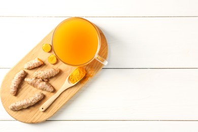 Photo of Aromatic turmeric tea in glass cup, roots and powder on white wooden table, top view. Space for text