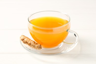 Photo of Aromatic turmeric tea in glass cup and root on white wooden table, closeup
