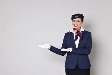 Photo of Smiling stewardess showing something on grey background. Space for text