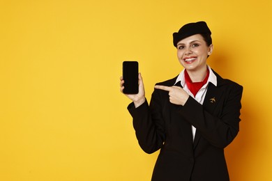 Photo of Smiling stewardess pointing at smartphone on orange background. Space for text