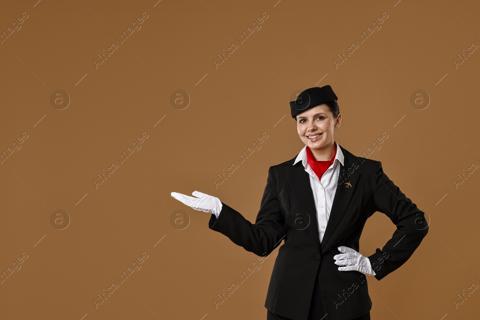 Photo of Smiling stewardess showing something on brown background. Space for text