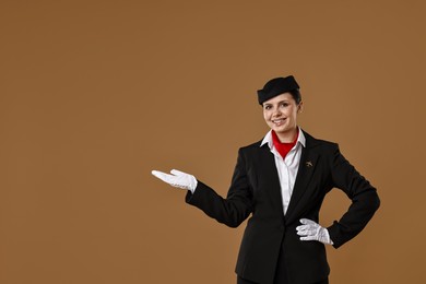 Photo of Smiling stewardess showing something on brown background. Space for text