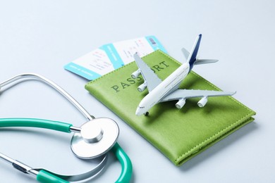 Photo of Medical tourism. Stethoscope, plane model, passport and flight tickets on light background