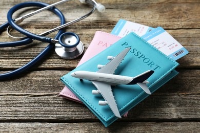 Photo of Medical tourism. Stethoscope, plane model, passports and flight tickets on wooden table, closeup