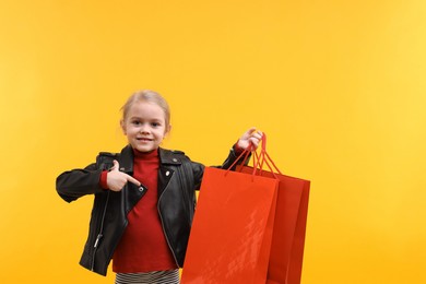 Photo of Little girl pointing at shopping bags on orange background