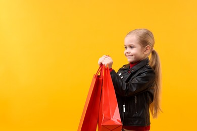 Photo of Little girl with shopping bags on orange background, space for text