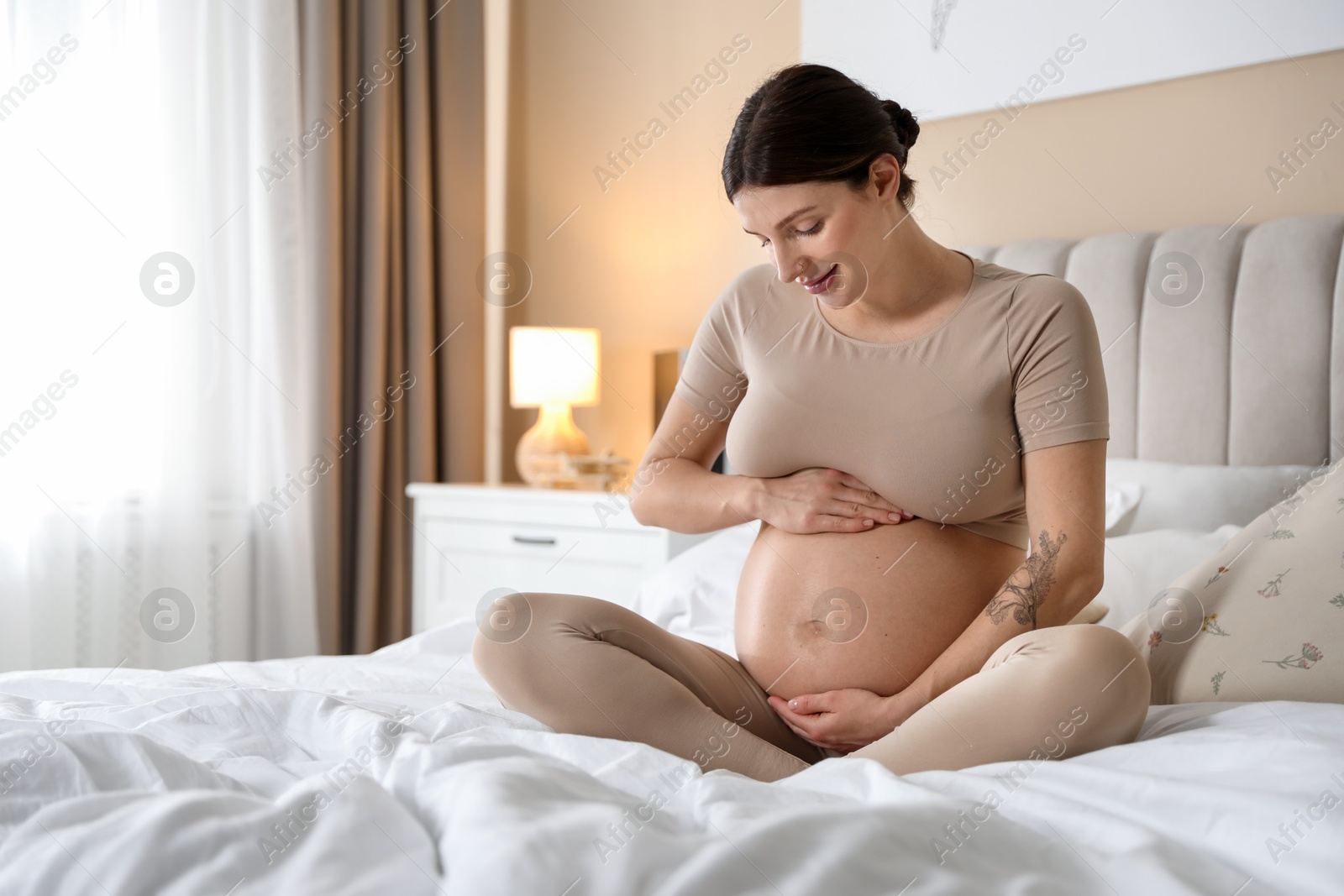 Photo of Beautiful pregnant woman on bed at home. Space for text