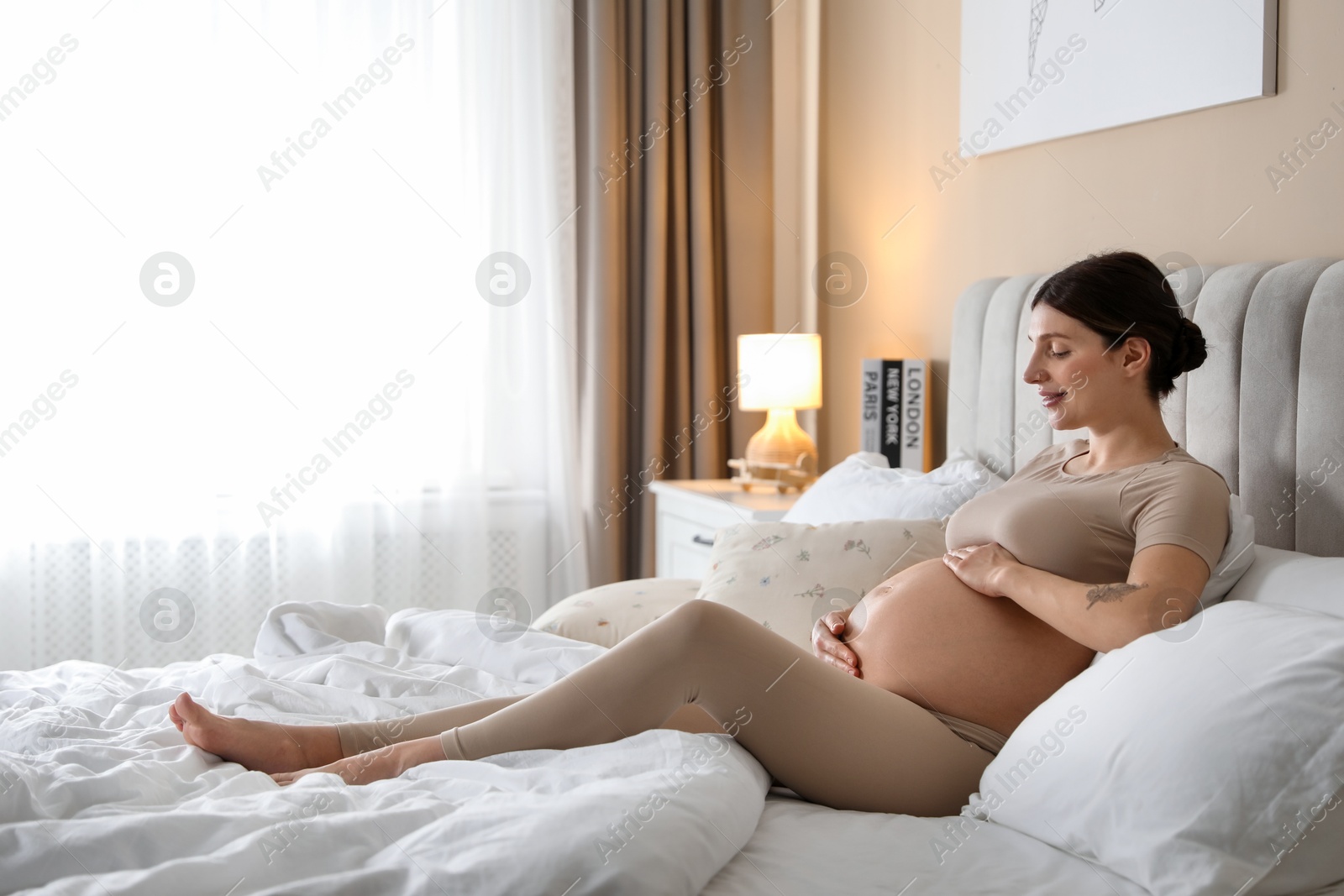 Photo of Beautiful pregnant woman on bed at home. Space for text