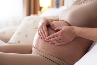 Photo of Pregnant woman making heart with hands on her belly at home, closeup. Space for text