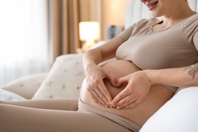 Photo of Pregnant woman making heart with hands on her belly at home, closeup. Space for text