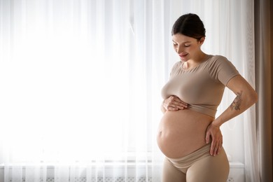 Photo of Beautiful pregnant woman near window at home. Space for text