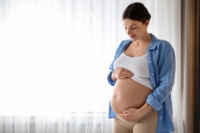 Photo of Beautiful pregnant woman near window at home. Space for text