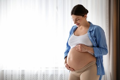 Photo of Beautiful pregnant woman near window at home. Space for text