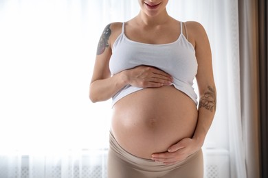 Pregnant woman near window at home, closeup. Space for text