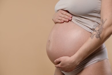 Photo of Pregnant woman with cute belly on beige background, closeup. Space for text