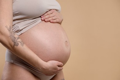 Photo of Pregnant woman with cute belly on beige background, closeup. Space for text