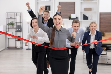 Photo of Competition concept. Happy businesswoman crossing red finish line ahead of her colleagues in office