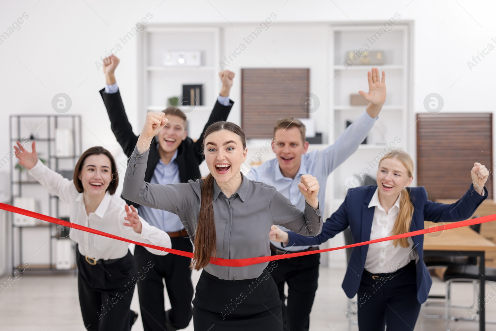 Photo of Competition concept. Happy businesswoman crossing red finish line ahead of her colleagues in office