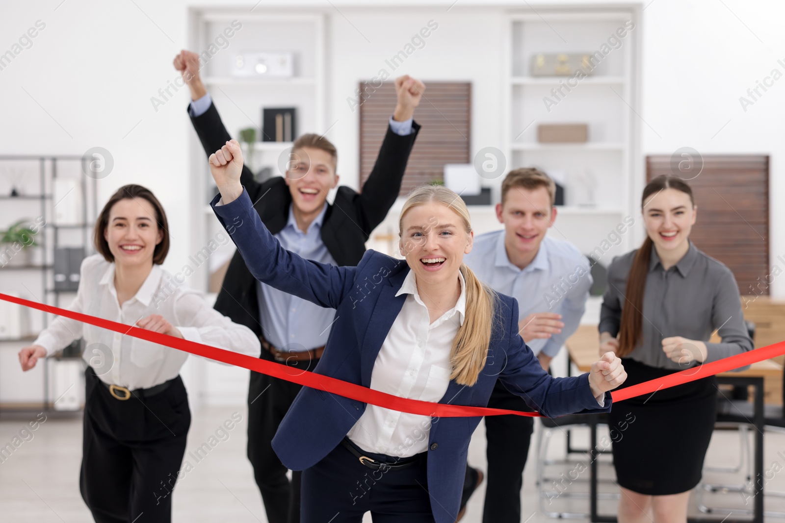 Photo of Competition concept. Happy businesswoman crossing red finish line ahead of her colleagues in office