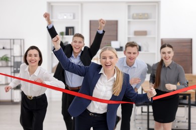 Photo of Competition concept. Happy businesswoman crossing red finish line ahead of her colleagues in office