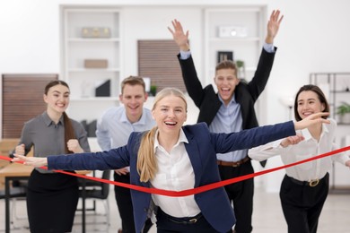 Photo of Competition concept. Happy businesswoman crossing red finish line ahead of her colleagues in office