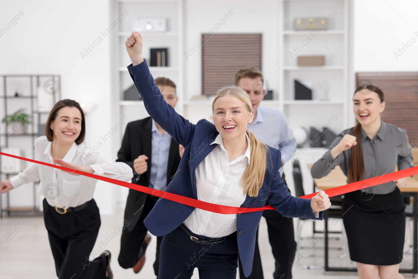 Photo of Competition concept. Happy businesswoman crossing red finish line ahead of her colleagues in office